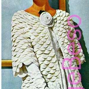 May include: A woman wearing a white crocheted dress and jacket with a large white flower brooch. The dress and jacket have a textured, scale-like pattern. She is wearing white gloves and white heels. The image is captioned "1960s".