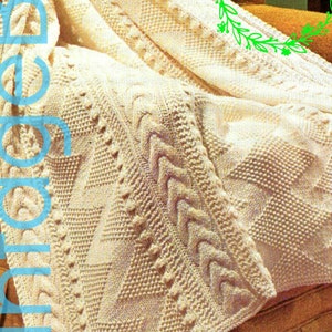 May include: A white knitted blanket with a cable knit pattern. The blanket is folded and draped over a chair. The text "1960s" is visible in the upper right corner of the image.