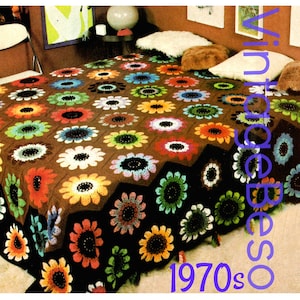 May include: A brown crocheted blanket with a pattern of colorful flowers. The blanket is on a bed with pillows and a side table.
