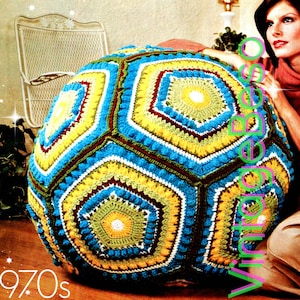May include: A large, crocheted, multi-colored, hexagonal-shaped floor pillow. The pillow is made with yellow, blue, green, white, and brown yarn. The pillow is sitting on a brown floor.