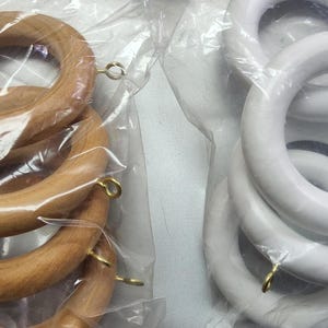 May include: Two sets of curtain rings, one set is natural wood and the other is white. Both sets are packaged in clear plastic bags.