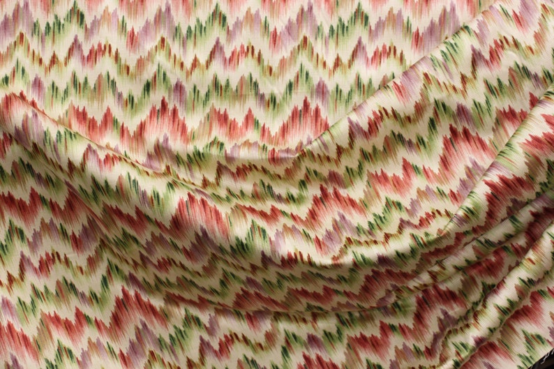 Op de afbeelding: Een close-up van een stof met een kleurrijk chevron-patroon. De stof is cr&egrave;mekleurig met rode, groene en paarse strepen.
