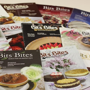 May include: A stack of colorful magazines with the title "Bits & Bites" on the covers. The magazines feature various food and recipes, including corn muffins, desserts, and a dish with a lamb shank.