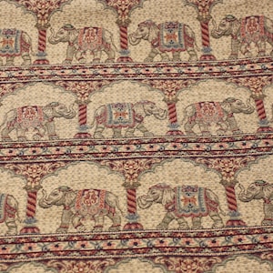 May include: Beige fabric with a repeating pattern of elephants walking under arches. The elephants are decorated with colourful floral designs and are outlined in brown. The arches are made of red and white stripes.