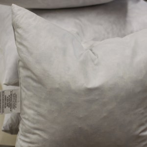 Puede incluir: Una pila de fundas de almohada blancas con una etiqueta pegada a una de las fundas de almohada.