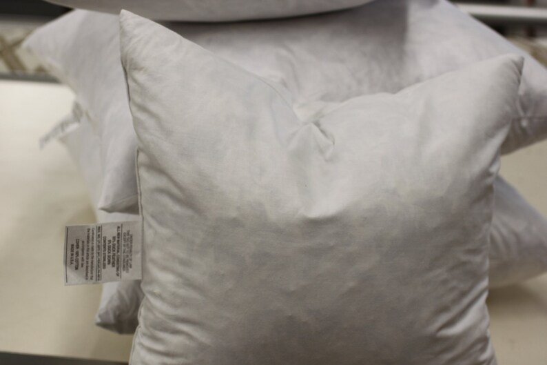 Puede incluir: Una pila de fundas de almohada blancas con una etiqueta pegada a una de las fundas de almohada.