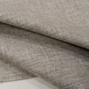 May include: Close-up of a beige woven fabric with a textured surface. The fabric is folded in half, showing the texture and weave.