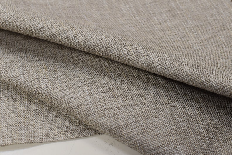 May include: Close-up of a beige woven fabric with a textured surface. The fabric is folded in half, showing the texture and weave.