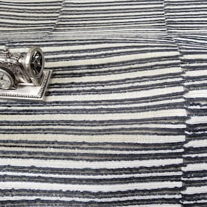 May include: A silver-colored miniature sewing machine clock sits on a striped black and white rug. The clock has a detailed design with a small clock face. The rug has a textured, horizontal striped pattern.