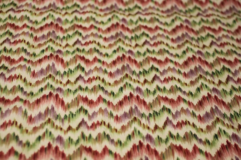 Op de afbeelding: Een stof met een chevron-patroon in tinten rood, groen, paars en wit.
