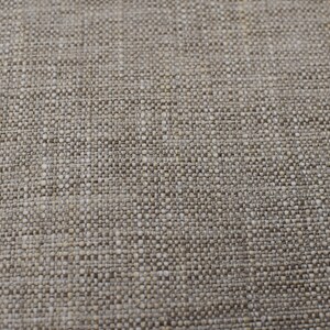 May include: A close-up of a beige textured fabric with a silver metal decorative piece in the bottom right corner.