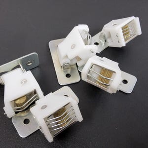 May include: Five white plastic curtain holdbacks with metal gears and a silver metal mounting plate.