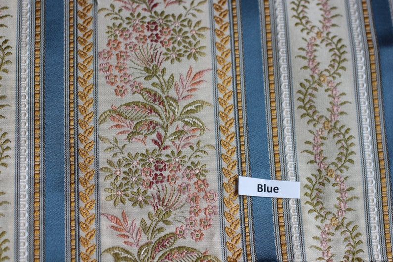 May include: Textile with a repeating pattern of vertical stripes in blue, gold, and cream. Floral and leaf motifs are interspersed between the stripes. The word "Blue" is on a white label.