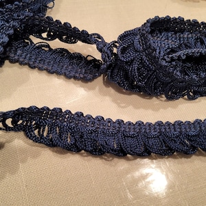 May include: A close-up of a dark blue crocheted trim with a scalloped edge. The trim is made of a soft, textured yarn and has a delicate, feminine look.