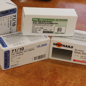 May include: Four boxes of staples, two are white with blue text and the words "True Fit" and "71/10" on them, one is white with green text and the words "beck Empire" and "22 go. Fine Wire Staples" on it, and one is white with orange text and the words "Spotnails" and "Galvanized Chisel Point Staples" on it.