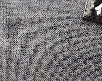 Op de afbeelding: Close-up van een textuurrijke, grijze stof met een subtiele blauwe tint. De stof heeft een geweven patroon en een licht ruwe textuur.