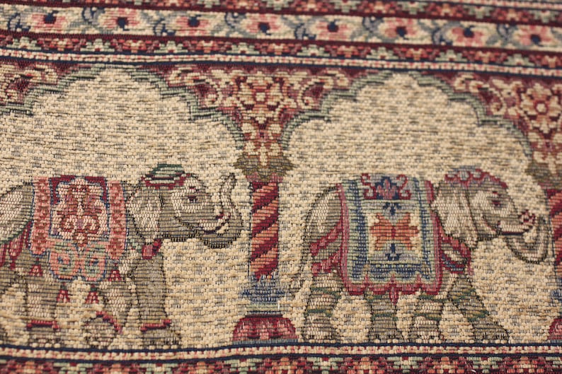 May include: A beige tapestry featuring a repeating pattern of elephants and floral designs. The elephants are carrying colourful saddle blankets and are walking under a stylised tree.