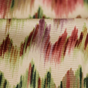 Op de afbeelding: Close-up van een cr&egrave;mekleurige stof met een geweven textuur. De stof heeft een abstract patroon in rood, groen en paarse tinten.