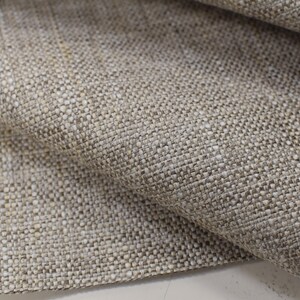 May include: Close-up of a beige linen fabric with a textured weave. The fabric has a subtle sheen and a slightly rough feel.