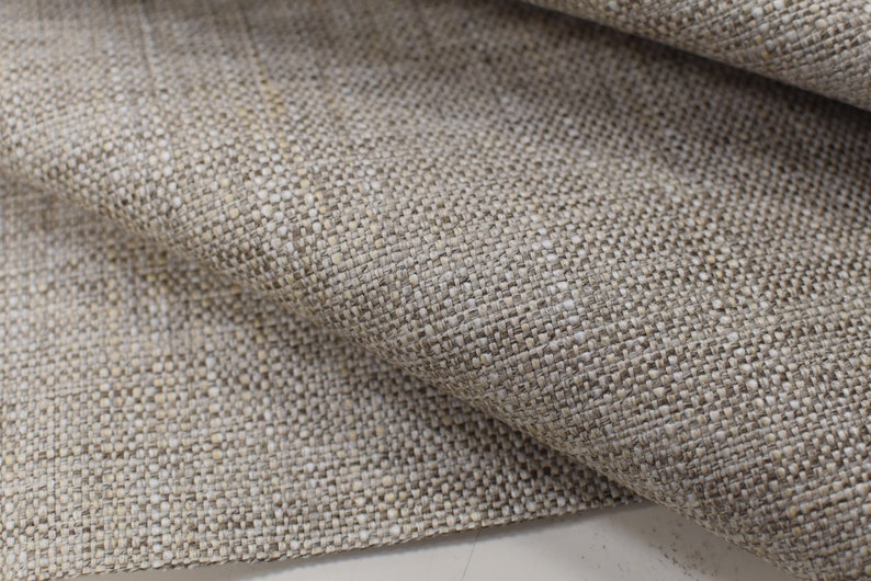 May include: Close-up of a beige linen fabric with a textured weave. The fabric has a subtle sheen and a slightly rough feel.
