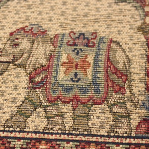 May include: A beige woven rug featuring a colourful elephant design. The elephant is outlined in blue and has a red, orange and green patterned saddle. The rug has a red, blue and green border.