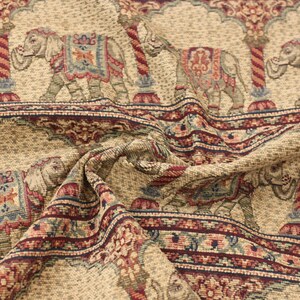 May include: Beige fabric with a repeating pattern of elephants in a tapestry style. The elephants are decorated with colourful floral designs and are standing under arches. The fabric has a textured, woven look.