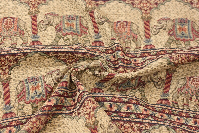 May include: Beige fabric with a repeating pattern of elephants in a tapestry style. The elephants are decorated with colourful floral designs and are standing under arches. The fabric has a textured, woven look.