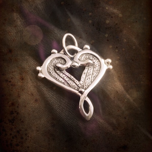 May include: A silver heart-shaped pendant with a detailed design, featuring a treble clef intertwined within the heart.