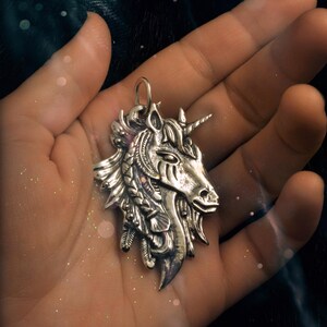 May include: A silver unicorn pendant with intricate details, including feathers and braids, hanging from a hand.