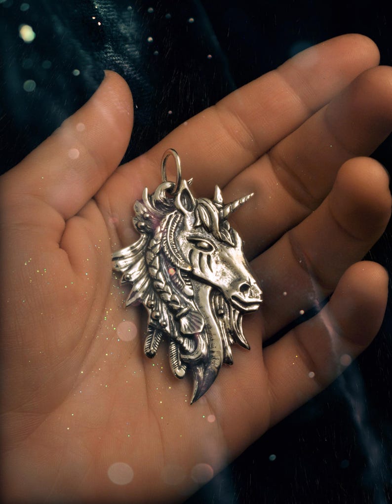 May include: A silver unicorn pendant with intricate details, including feathers and braids, hanging from a hand.