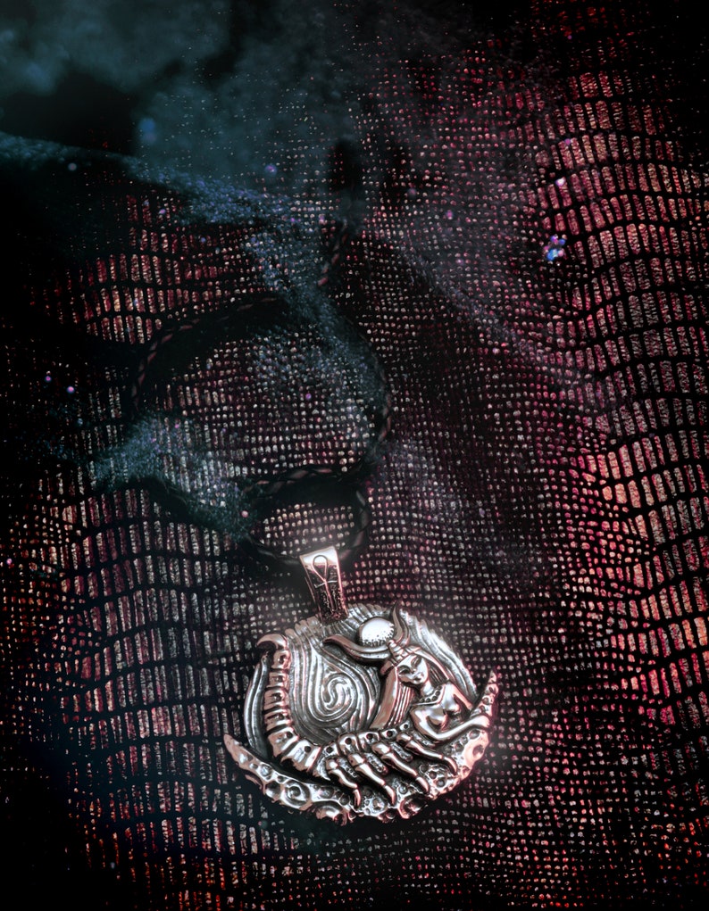 May include: Silver pendant necklace with a detailed design of a woman holding a scorpion. The pendant is on a black leather cord and is set against a dark red background.
