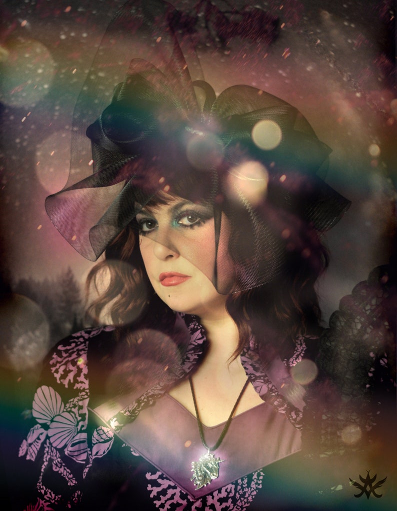 May include: A woman wearing a black lace veil and a purple dress with a silver pendant necklace. The background is blurred and has a soft, dreamy effect.