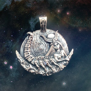 May include: A silver pendant featuring a detailed depiction of a woman with a scorpion tail, set against a crescent moon background. The pendant has an ankh symbol at the top.