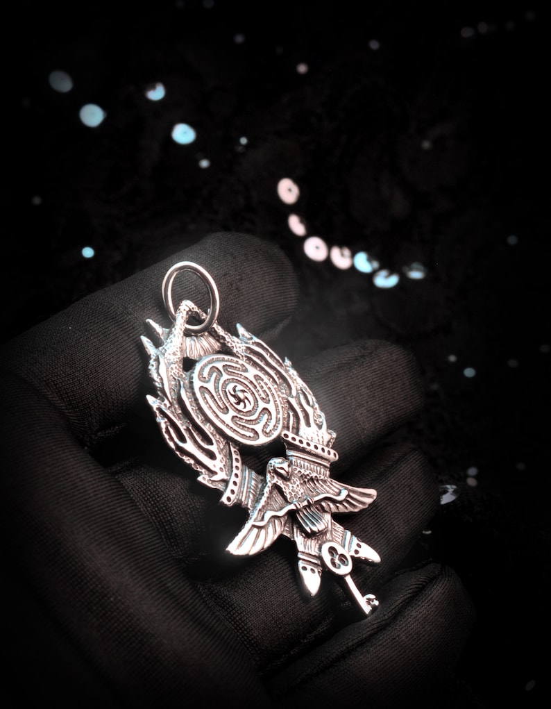 May include: A silver pendant featuring a stylized bird with a key and a circular design with a maze pattern.