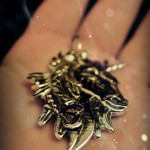 May include: A silver unicorn pendant with intricate details, featuring a detailed head and horn. The pendant is on a person's hand.