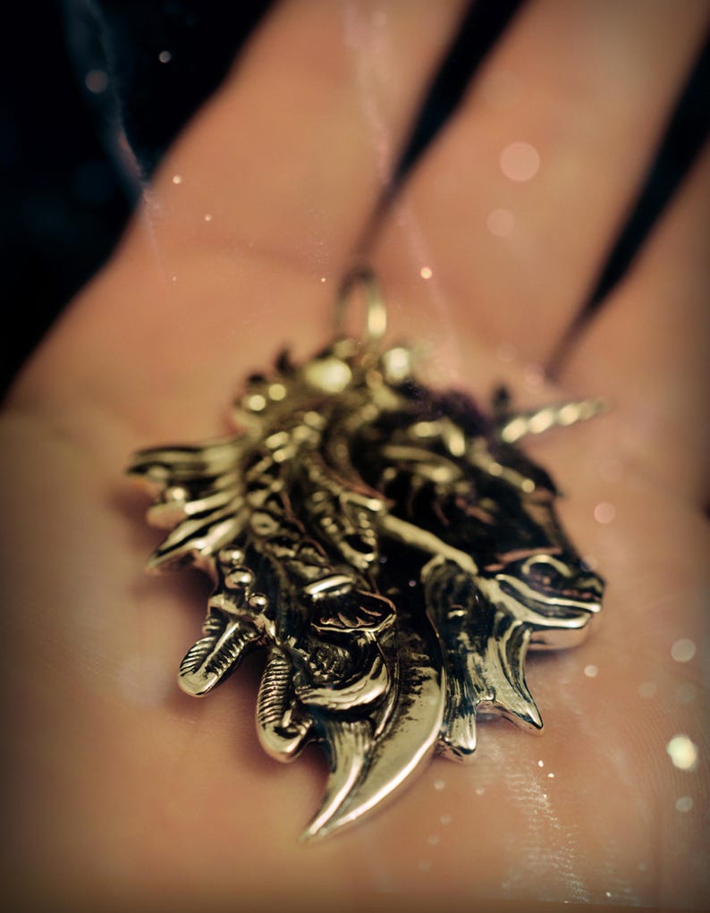 May include: A silver unicorn pendant with intricate details, featuring a detailed head and horn. The pendant is on a person's hand.