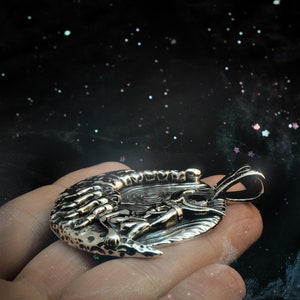May include: A silver pendant featuring a detailed design of a scorpion curled around a crescent moon.