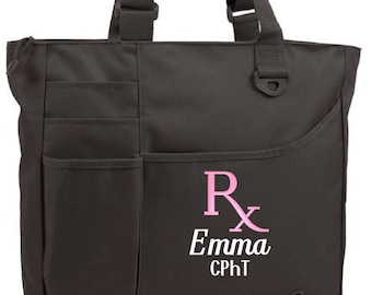 May include: Black tote bag with a large front pocket and a smaller pocket on the side. The bag has a pink embroidered Rx symbol, the name Emma, and the letters CPHt.