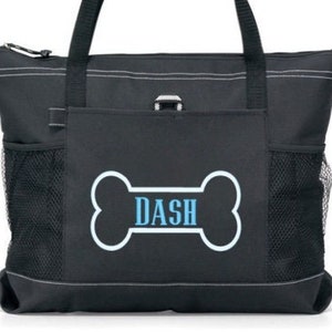 May include: Black tote bag with a white bone-shaped design and the name "DASH" in blue text. The bag has a zipper closure, two side pockets, and a front pocket.