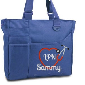 Pode incluir: Uma bolsa tote azul com um bolso grande na frente. A bolsa tem um cora&ccedil;&atilde;o vermelho com um estetosc&oacute;pio e o texto "LPN Sammy" bordado.