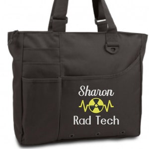 May include: A dark brown tote bag with multiple exterior pockets and a shoulder strap. The bag features the text "Sharon Rad Tech" with a yellow radiation symbol and heartbeat graphic.