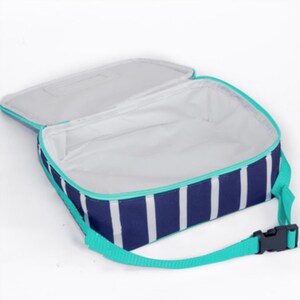 May include: A rectangular lunch bag with a navy blue and white vertical striped pattern. The bag features a bright turquoise zipper trim and an adjustable turquoise strap with a black plastic buckle. The interior is lined with white material.