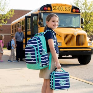May include: A navy blue and white horizontal striped backpack and matching lunch bag with teal trim and a teal monogrammed design. The backpack features a side pocket holding a clear water bottle, and both items have silver zippers and hardware.