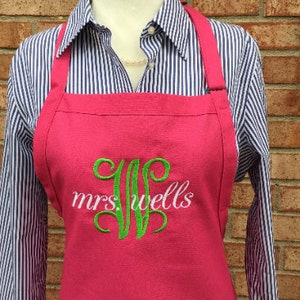 Pu&ograve; includere: Un grembiule rosa con spalline regolabili e un monogramma ricamato in verde che dice "mrs. wells"