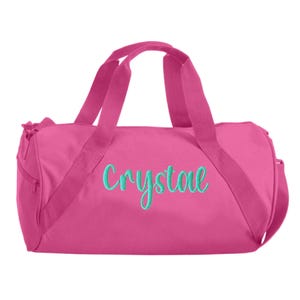 May include: Pink duffel bag with a teal embroidered name "Crystal" on the front.