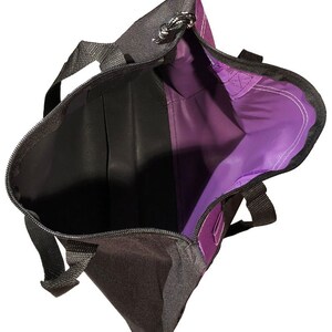 May include: A purple and black tote bag with a zip closure and two handles. The bag is open and the inside is visible.
