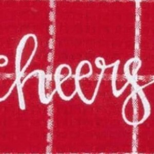 May include: A close-up of a red background with a white plaid pattern. The word "cheers" is written in a cursive font across the center of the image. The image is a festive design.