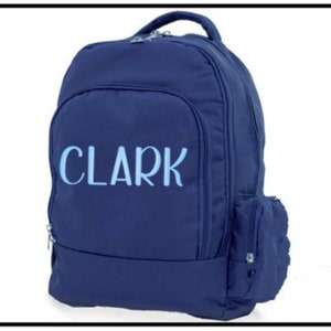 May include: A navy blue backpack with a zippered front pocket and the name "CLARK" embroidered in light blue on the front.
