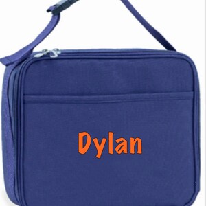 May include: A blue insulated lunch bag with a zipper closure and an adjustable shoulder strap. The bag has a front pocket and the name "Dylan" is embroidered on the front in orange.