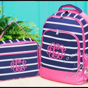 May include: A navy blue and white striped backpack and matching lunch bag set with bright pink trim and zippers. Both items feature a pink embroidered monogram of the letter C on the front. The backpack includes a top handle and side pockets.
